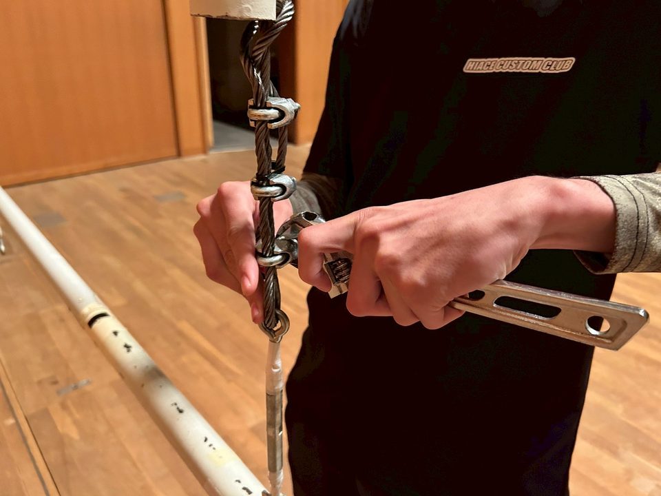 舞台設備のワイヤー金具を工具で点検する様子